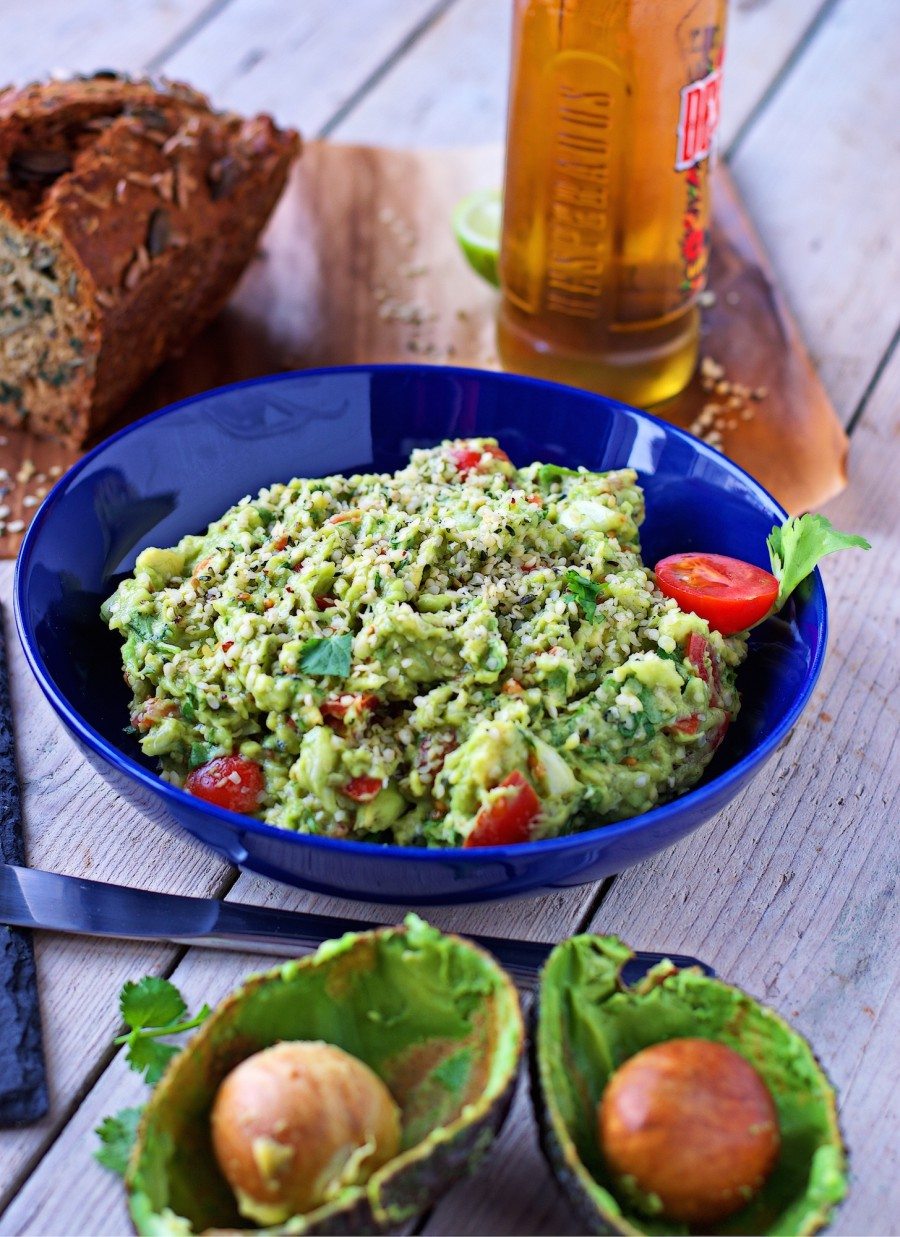 A large bowl full of the Hemp Guacamole with two empty avocado halves in the foreground.