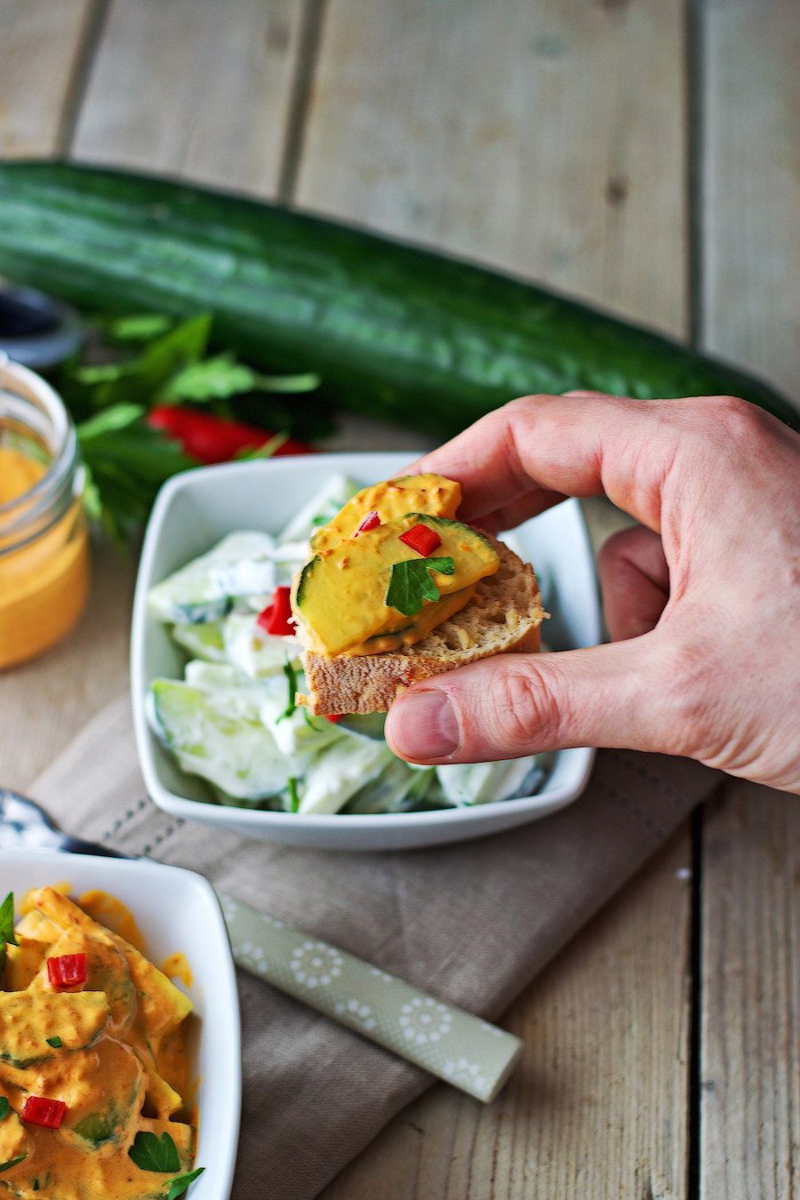 A hand holding a piece of bread with the spicy cucumber salad.