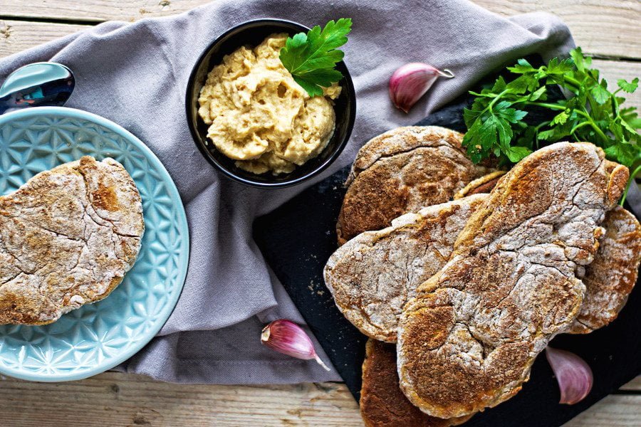 A serving plate with several Easy Roasted Garlic Naan breads and a small bowl of hummus on a decorative cloth. 