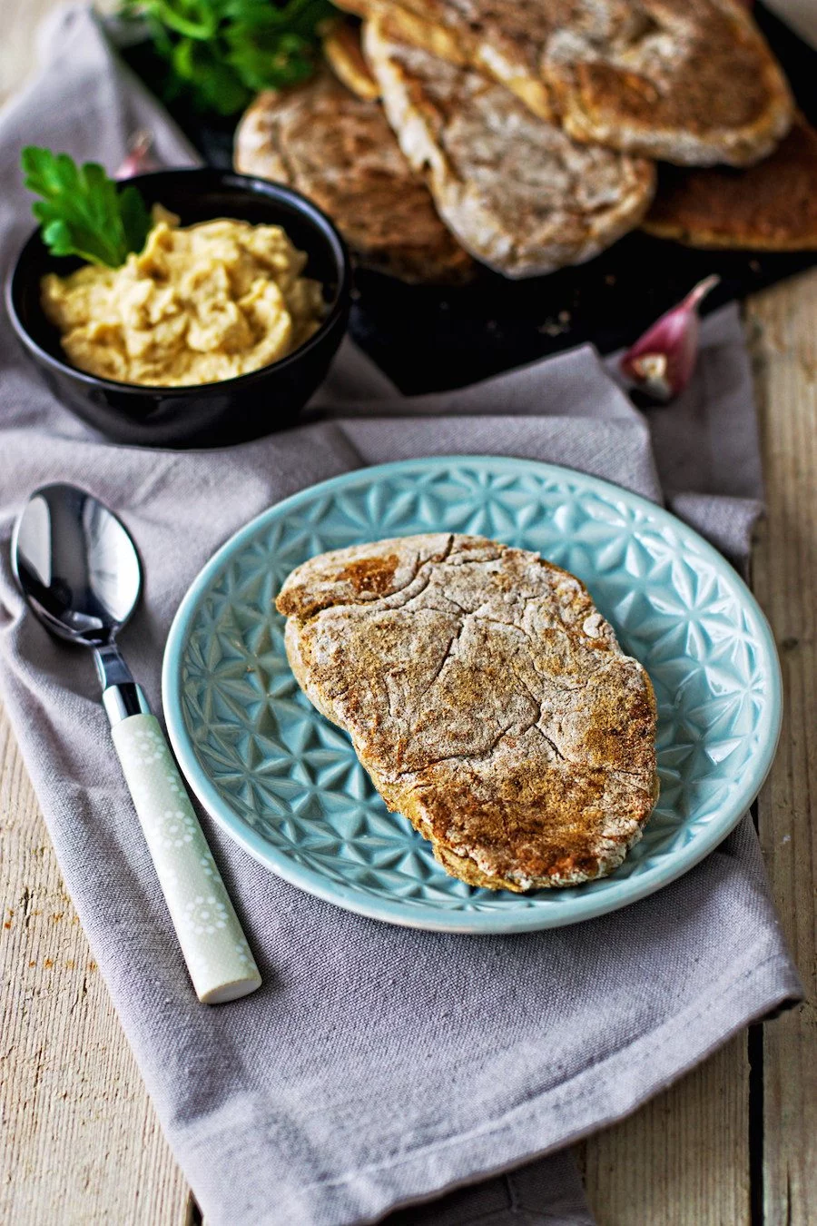 A single Garlic Naan on a small blue plate, with a spoon at its side.