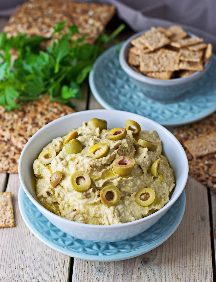 A portion of the Olive Hummus in a white bowl, garnished with extra green olive slices.