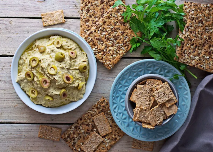 Top view on a bowl of the Olive Hummus and a bowl of the vegan crackers for dipping.