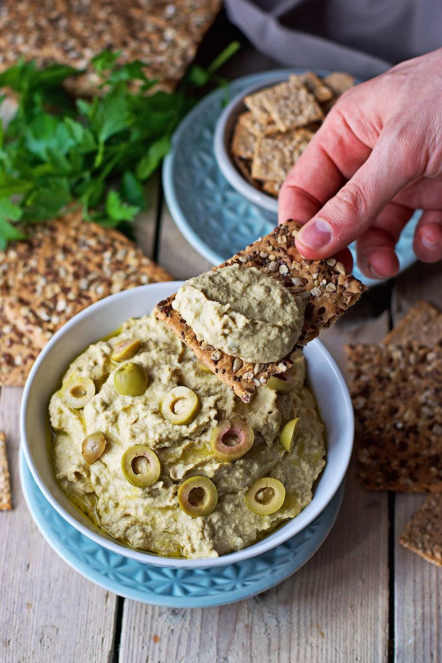 A wholegrain cracker, dipped into olive hummus.