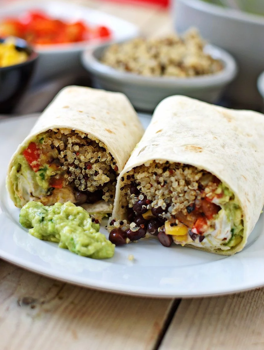 Two Mexican Quinoa Wrap halves side-by-side on the white plate with a spoon of guacamole.