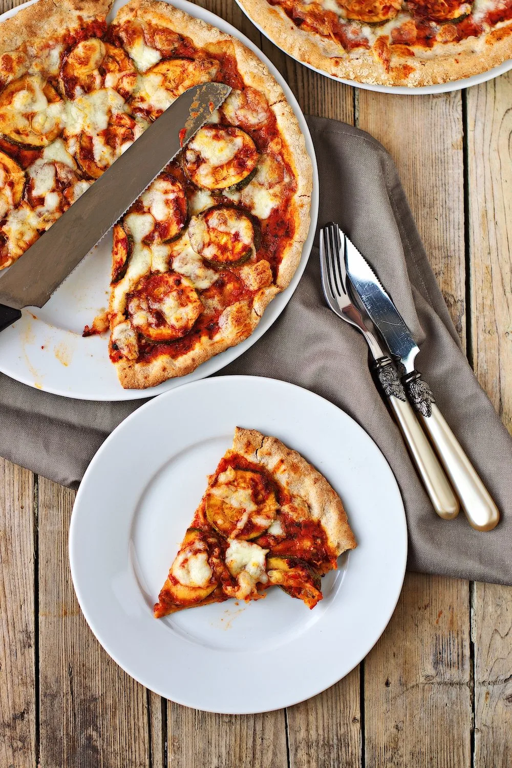 Top view on a Vegan Pepperoni Pizza with a slice taken out and on a plate set on a decorative cloth.