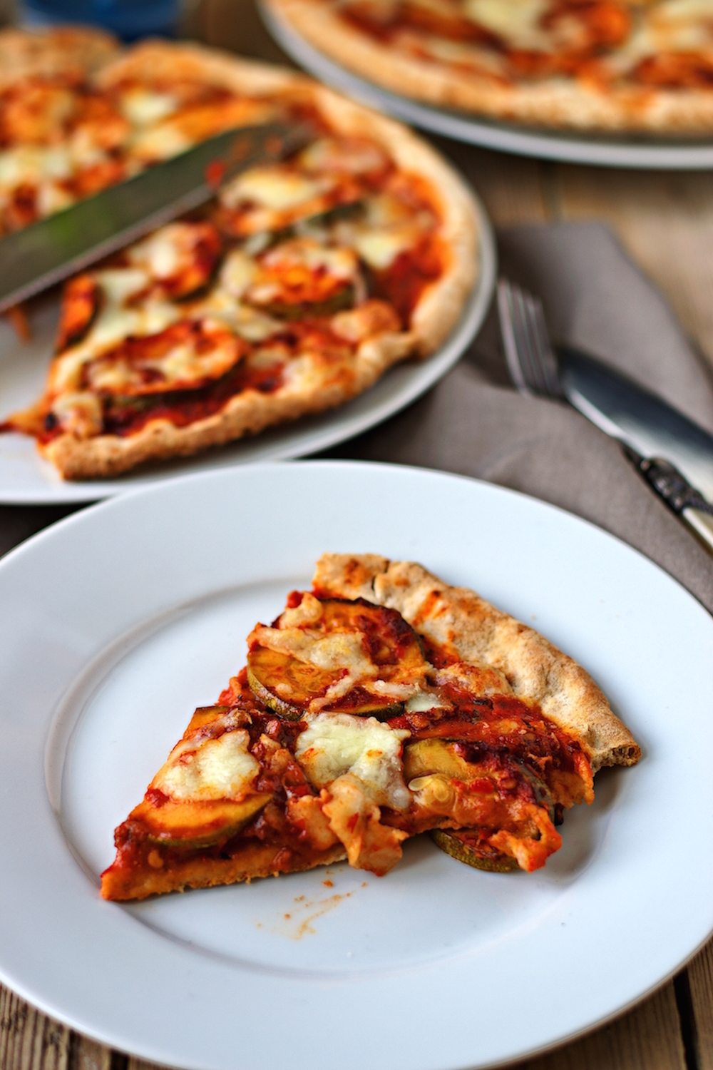 A slice of the Vegan Pepperoni Pizza on a small white plate with the rest of the pizza in the background.