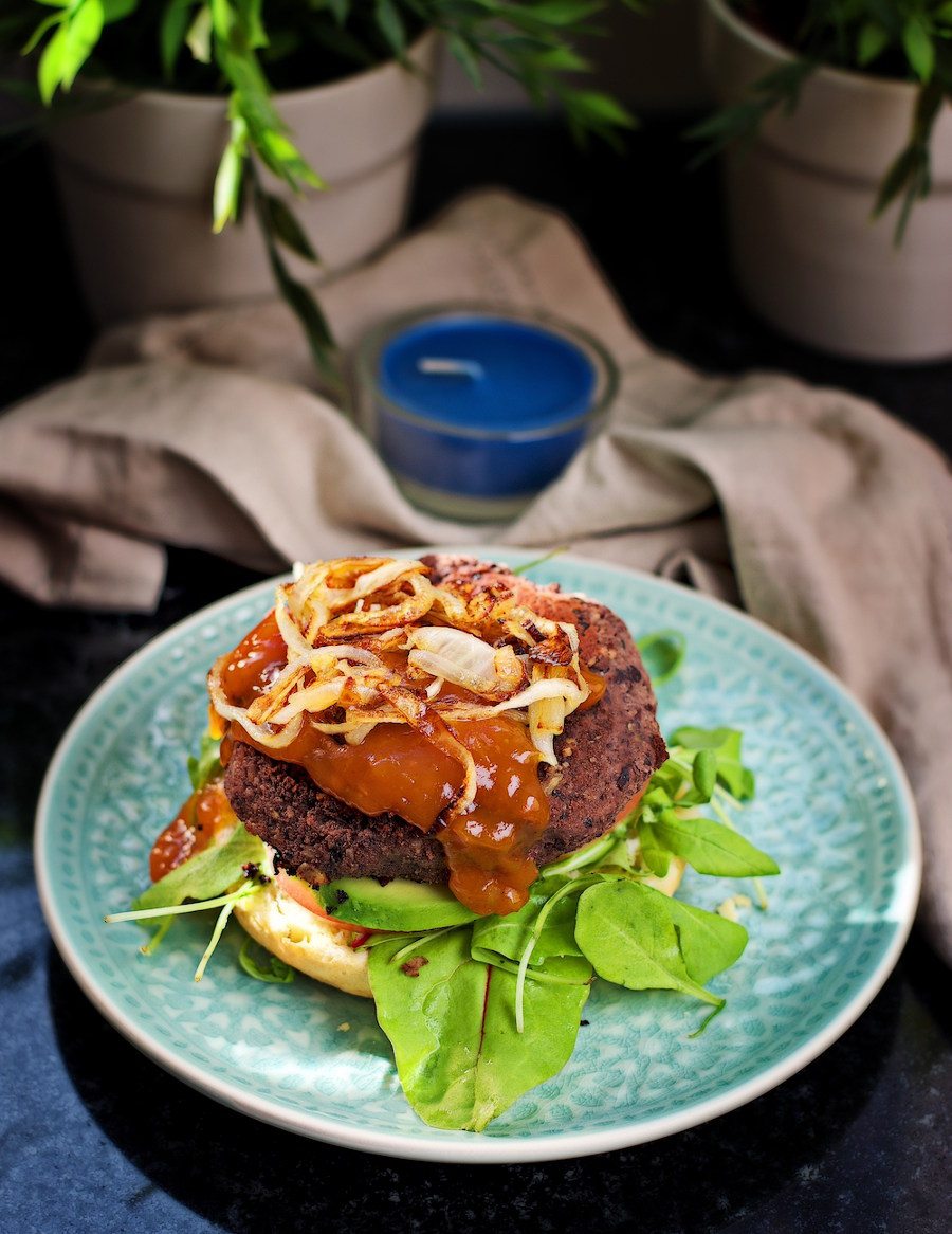 An open Vegan Black Bean Burger with sauce and fried onions.