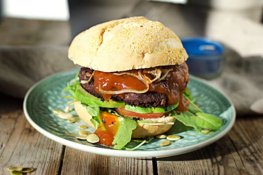 The Vegan Black Bean Burger is juicy with sauce dripping out.