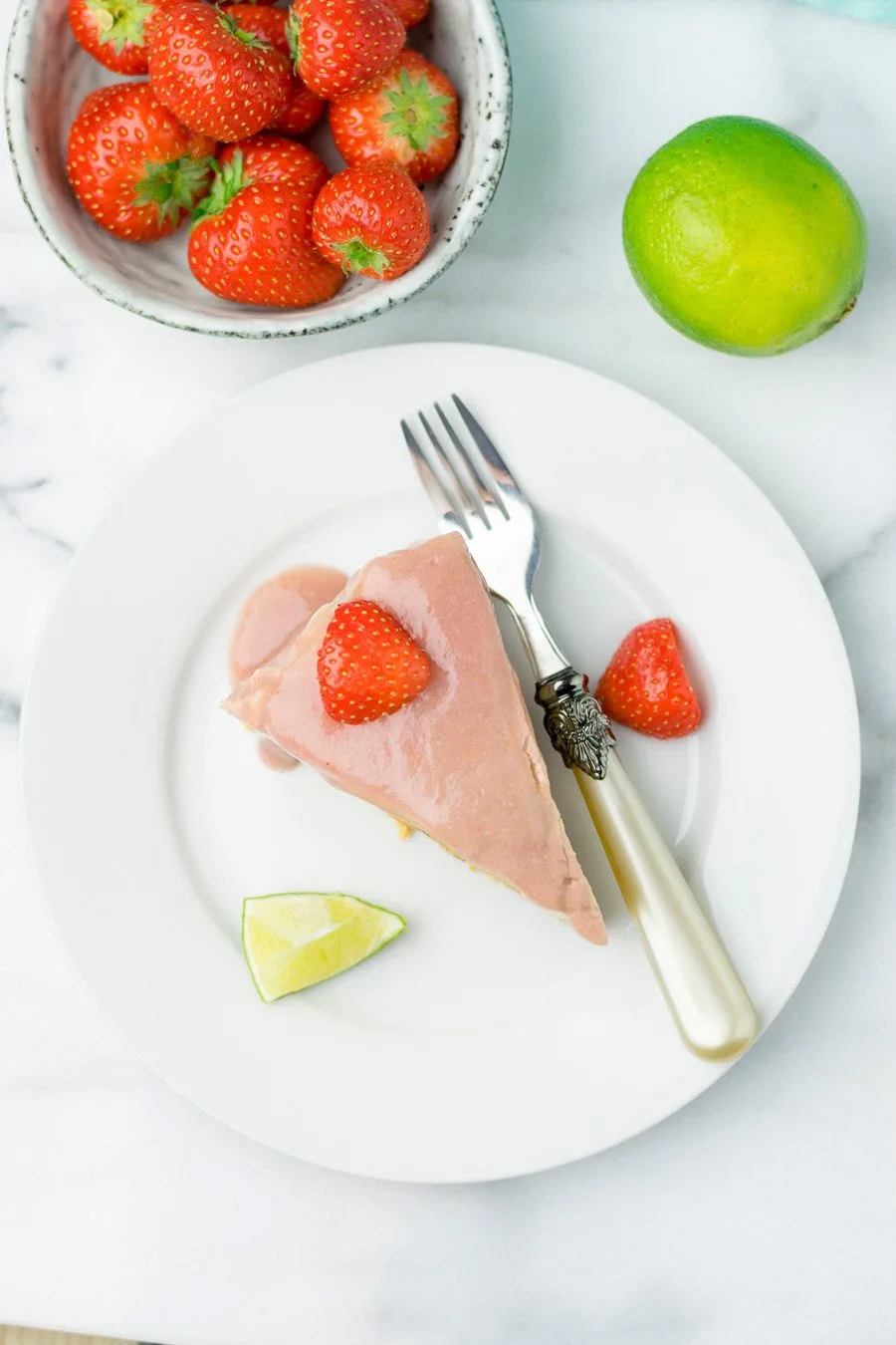 Top view on a slice of Raw Vegan Strawberry Peanut Butter Cheesecake on a plate with a fork, with extra strawberries in the background.