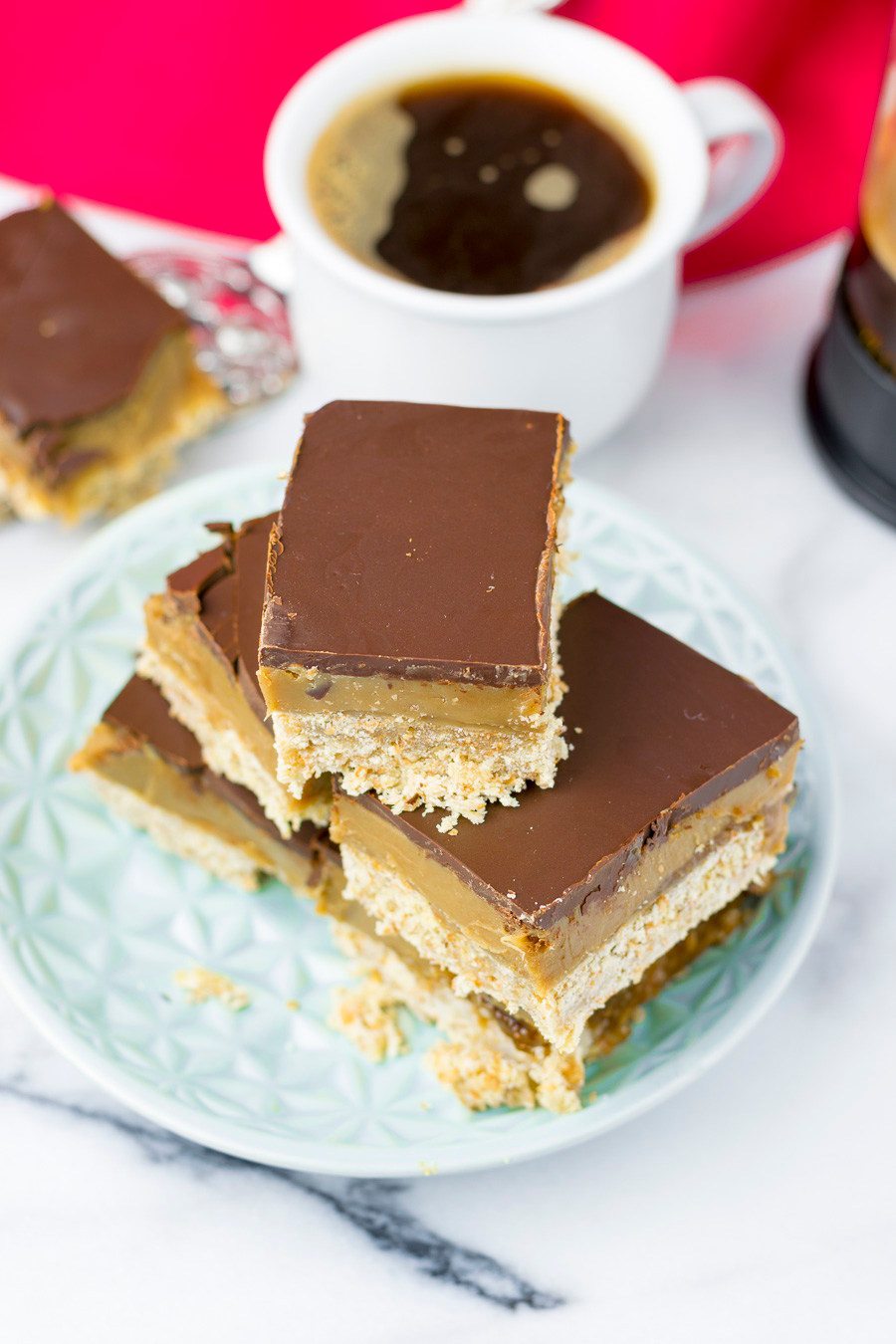 Top view on the caramel shortbread, showing the chocolate top, a cup of coffee in the background.