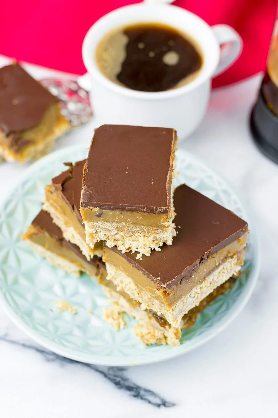 Top view on the caramel shortbread, showing the chocolate top, a cup of coffee in the background.