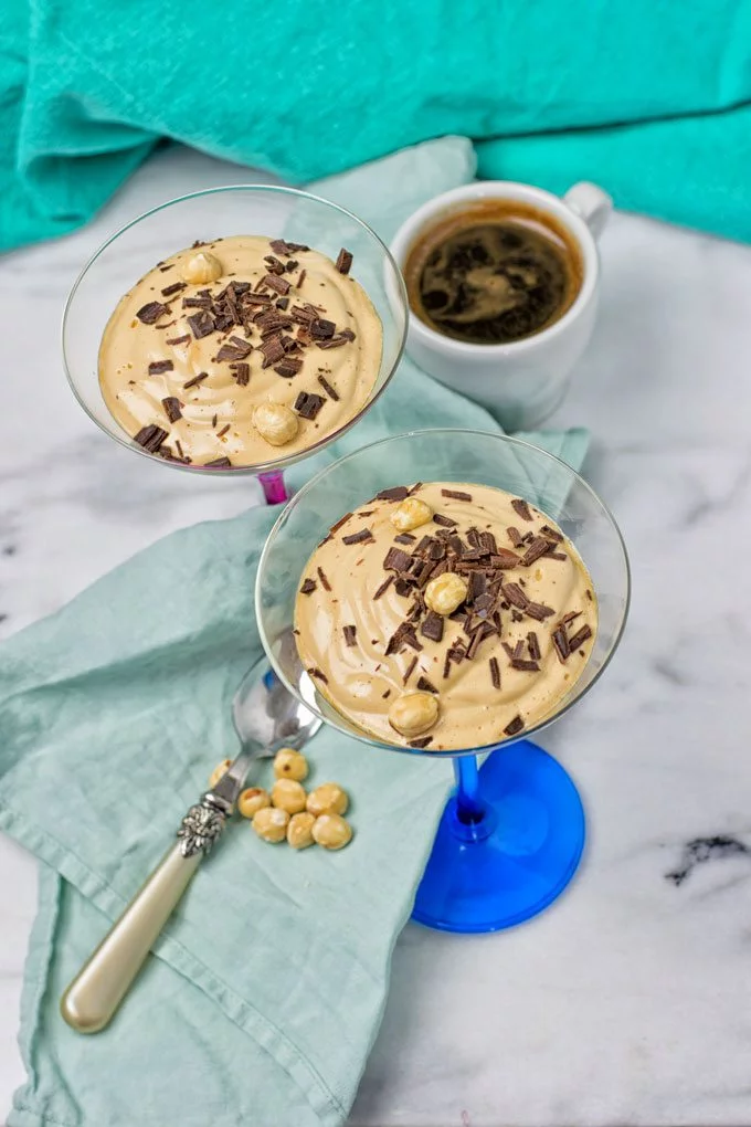 Two servings of the Coffee Cheesecake Mousse in cocktail glasses with a cup of coffee in the background.