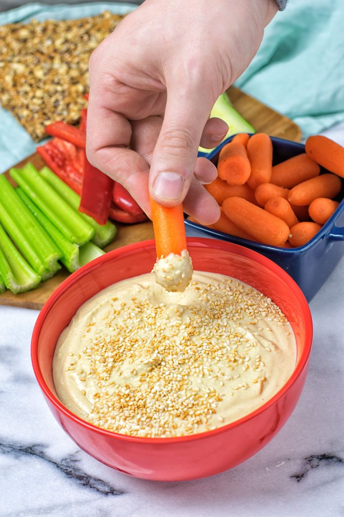 Hand dipping a carrot into the hummus