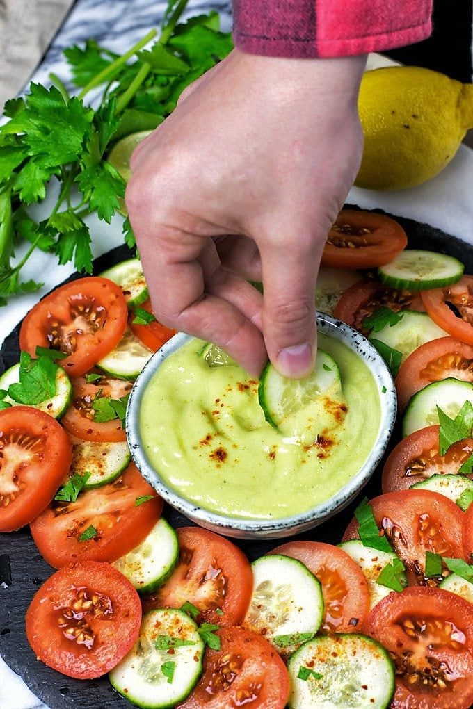 Hand dipping a cucumber slice into the Everyday Detox Dipping Sauce.