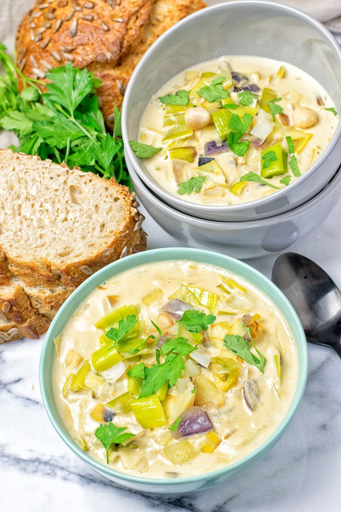 Two bowls of the Vegan Cheese Leek Soup with bread in the background.