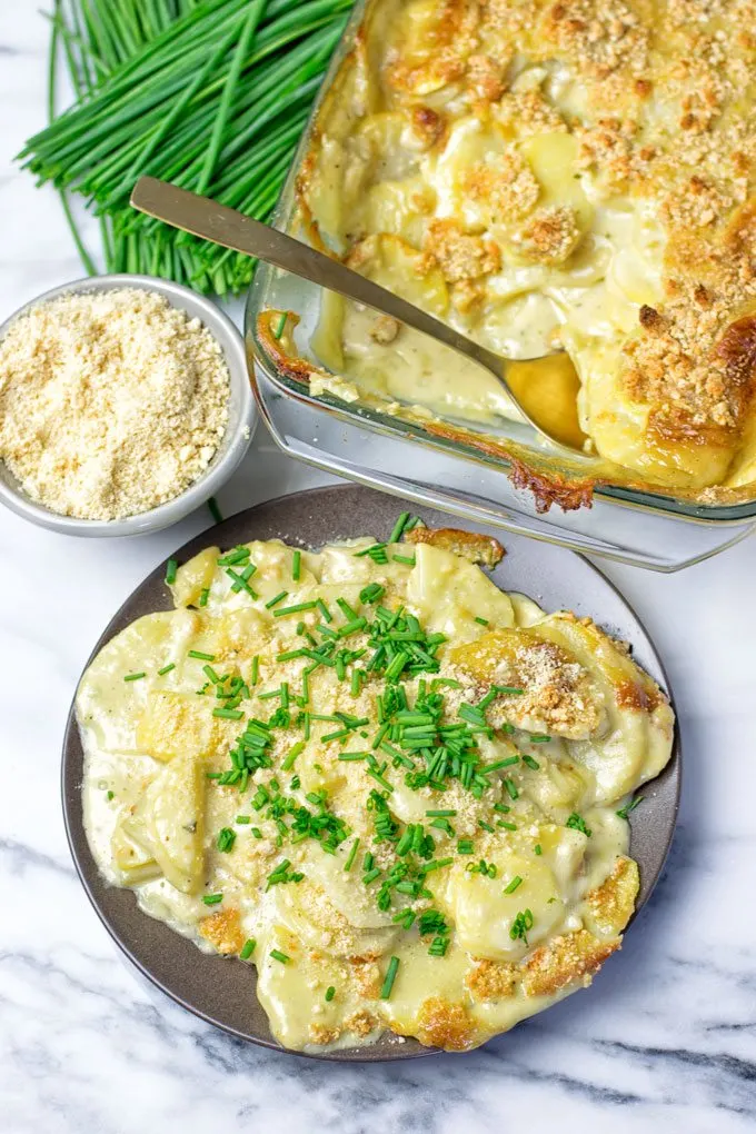 A plate of the Garlic Butter Scalloped Potatoes with the baking dish in the background.