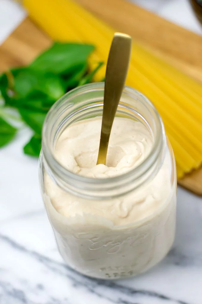 The Spicy Tahini Pasta Sauce in an open glass jar with a golden spoon.