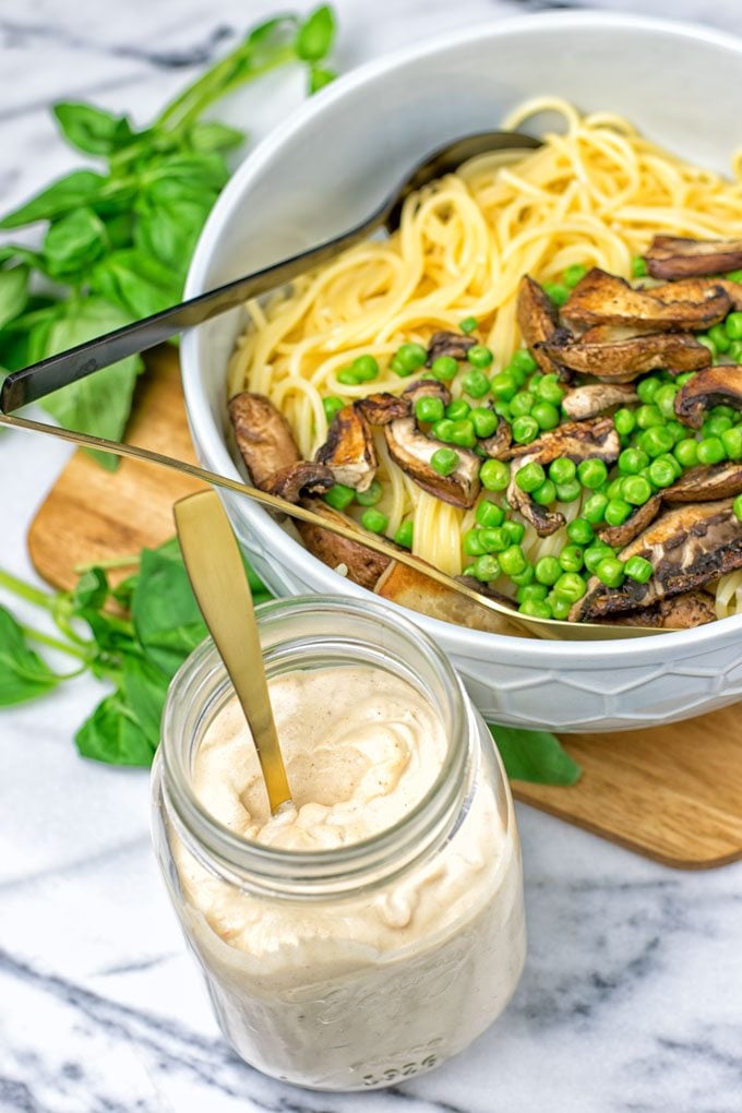 Spicy Tahini Pasta Sauce jar with a bowl with pasta in the background.