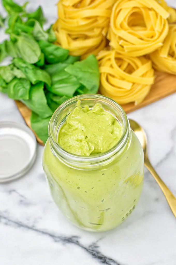 Open Avocado Pesto Pasta Sauce with uncooked pasta a fresh basil in the background.