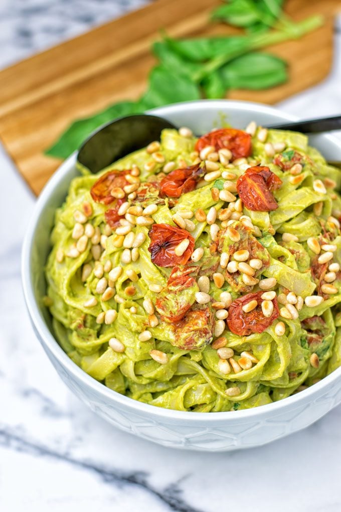 A bowl of pasta mixed with the Avocado Pesto Sauce garnished with sun-dried tomatoes and toasted pine nuts.