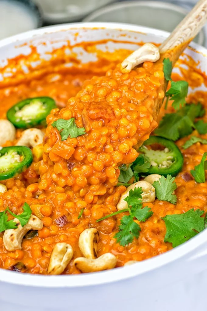 A large wooden spoon lifts some Lentil Dal from the pot.