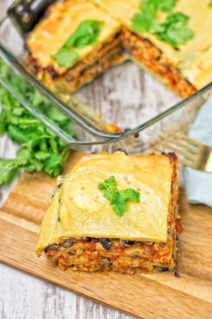 A piece of the Easy Vegan Taco Lasagna on a wood board with the casserole dish in the background.