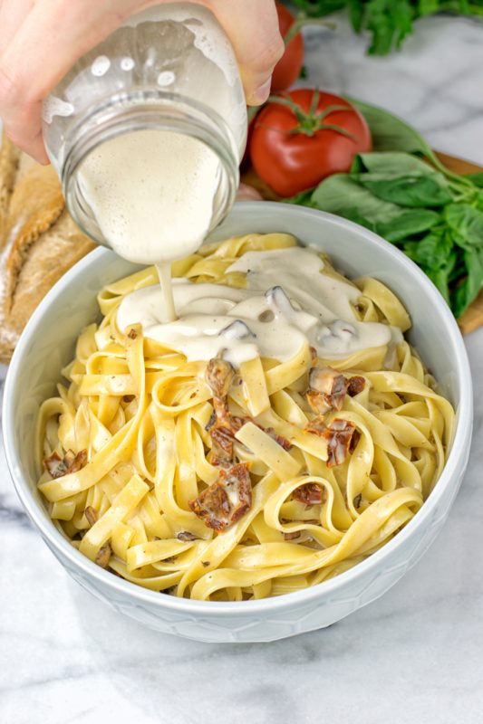 Pouring the Roasted Garlic Carbonara Sauce from the jar over pasta.