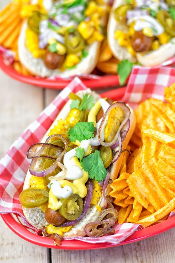 A Mexican Street Corn Hot Dogs with a side of potato chips.