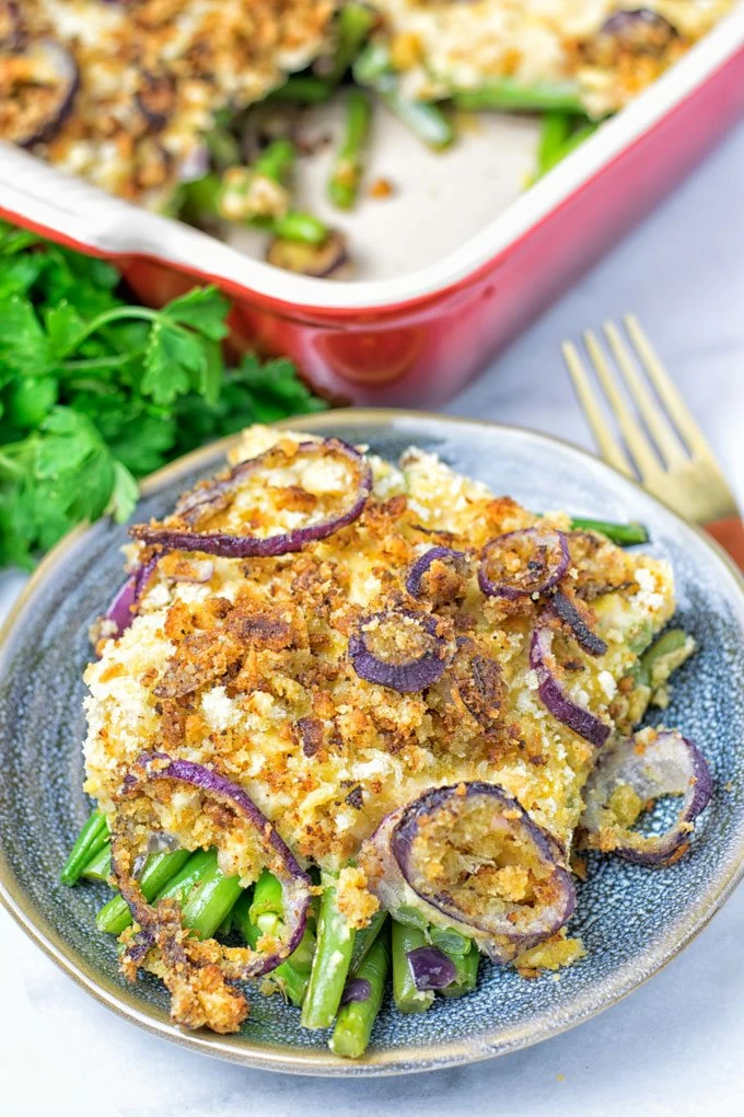 A portion of the Chickpea Mash Green Bean Casserole on a blue plate with the casserole dish in the background.