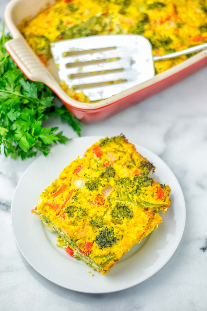 Piece of the crustless quiche on a white plate with the red casserole dish in the background.