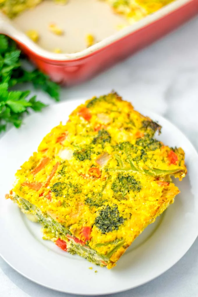 Closeup of a piece of the crustless quiche on a white plate with the red casserole.