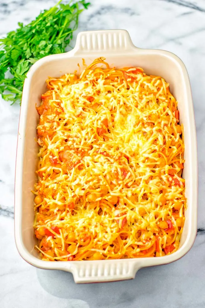 View of baked spaghetti casserole in the dish with fresh parsley in the background.