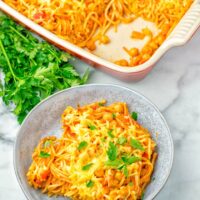 Vegan Spaghetti casserole portion dressed with parsley. Background red casserole dish.