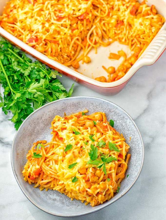Vegan Spaghetti casserole portion dressed with parsley. Background red casserole dish.