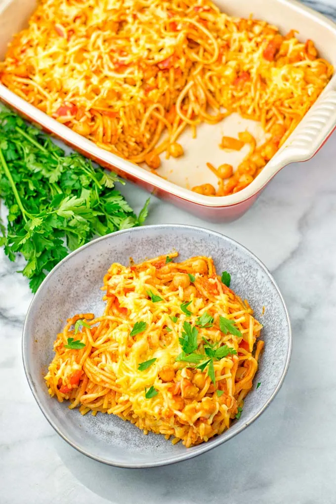 Vegan Spaghetti casserole portion dressed with parsley. Background red casserole dish.