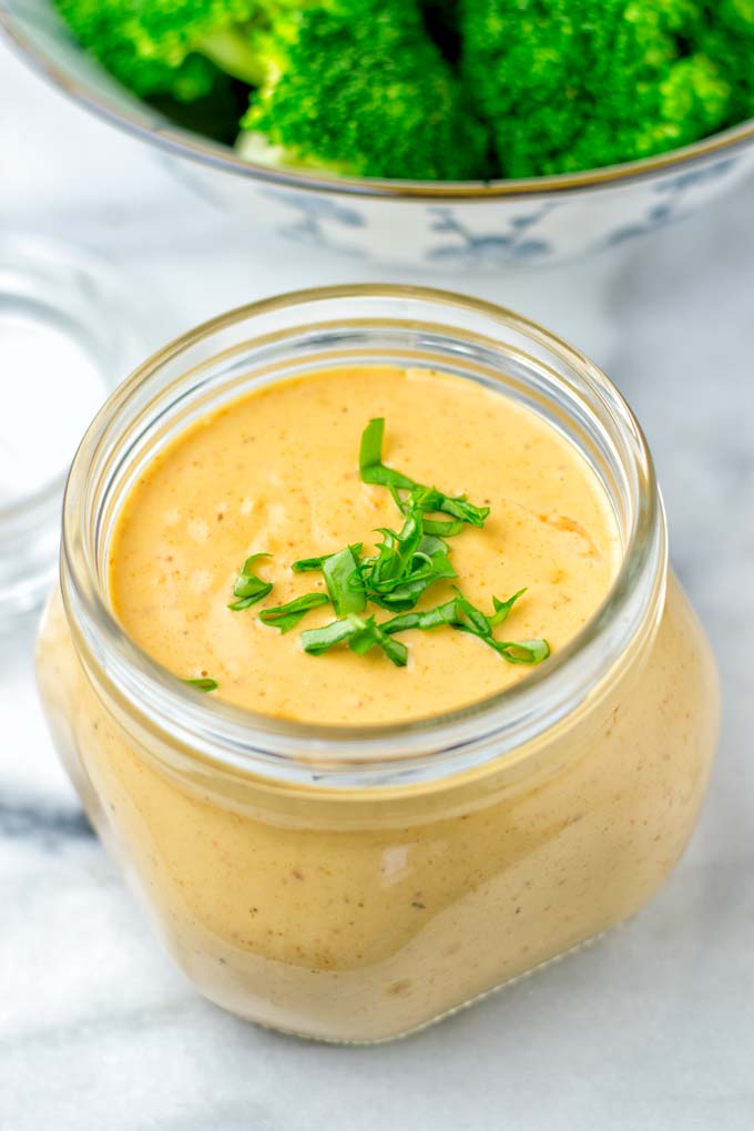 Thai Peanut Sauce in a jar topped with basil with broccoli in the background.