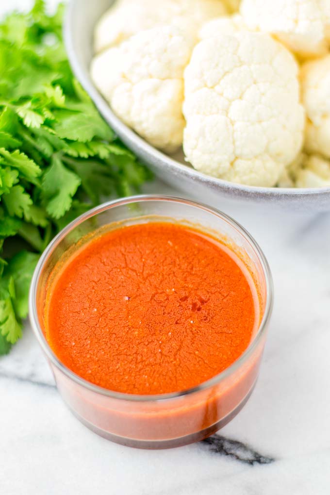 Buffalo Sauce in a glass bowl with cauliflower in the background.