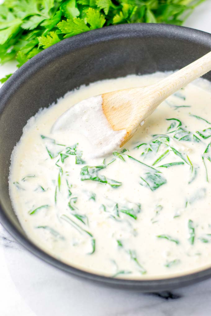 Sauce is cooking in a small saucepan, being stirred with a wooden spoon.