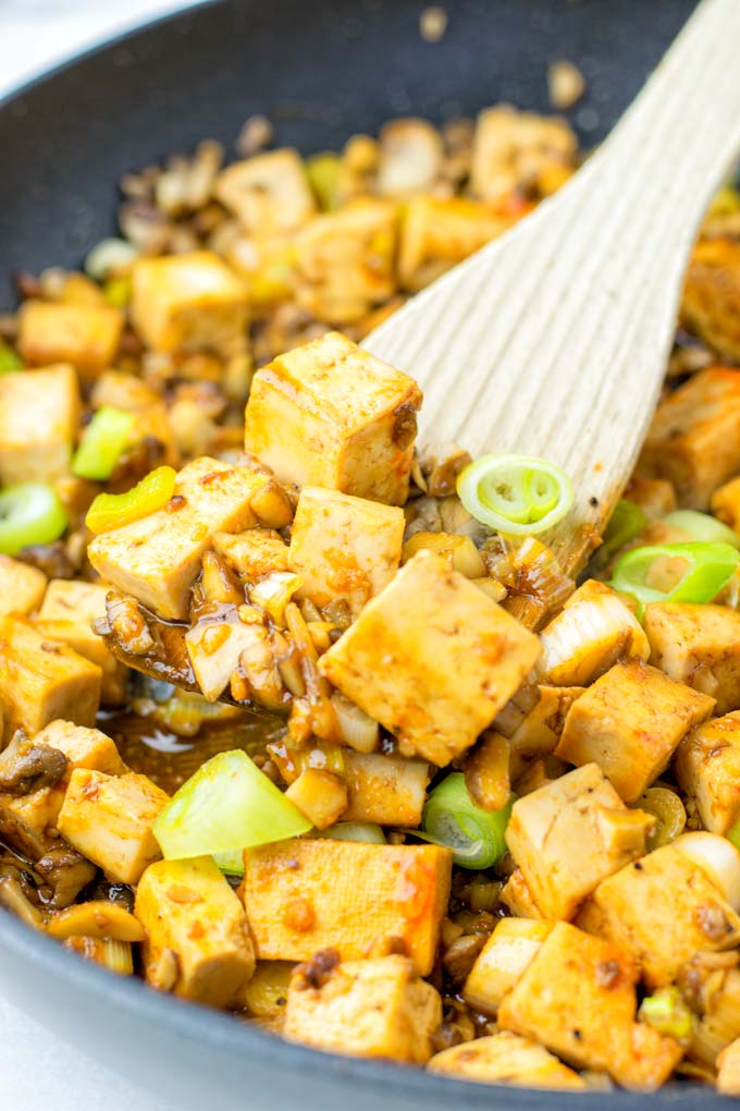 A wooden spoon lifts up some tofu cubes and mushroom 'meat'.