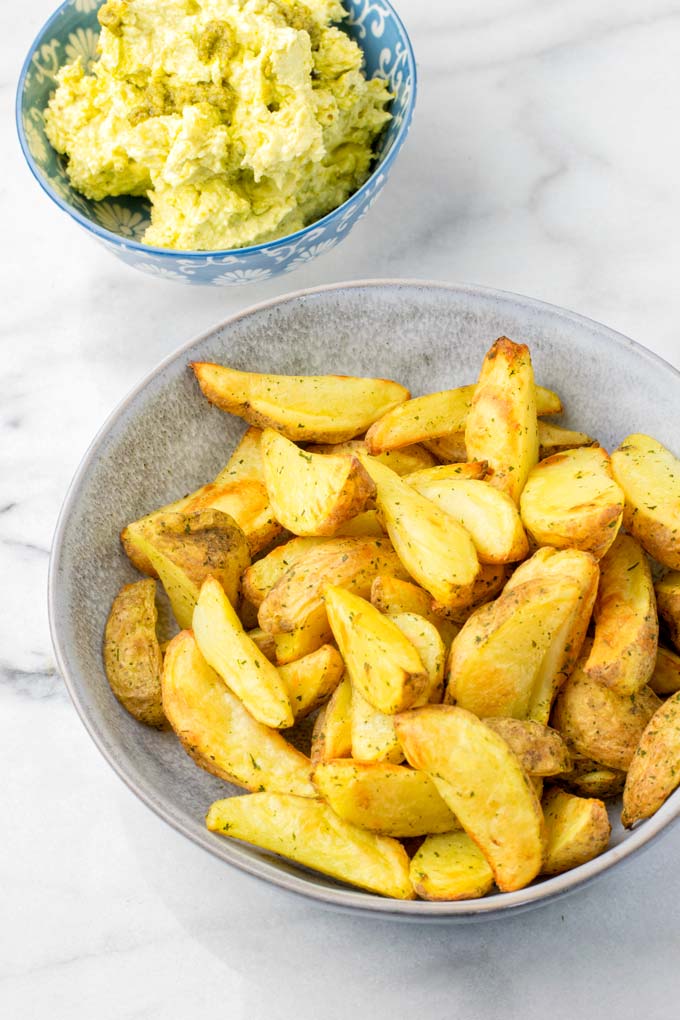 A bowlful of potato wedges in front of the ready pesto butter.