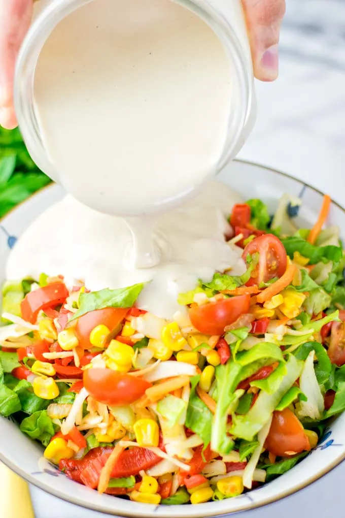 Tahini Dressing is poured from the jar onto a fresh salad.