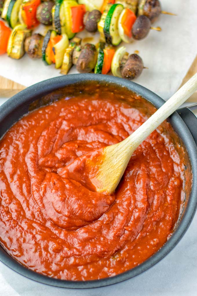 The BBQ sauce is simmering in a small wide sauce pan, being whisked with a wooden spoon.