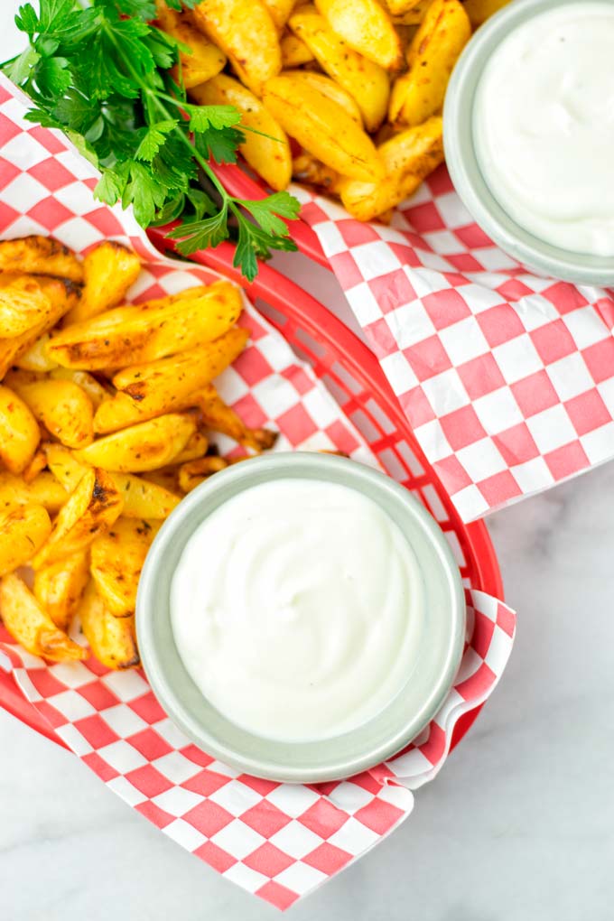 Small bowl of White BBQ sauce in a red basket with roasted potato wedges.