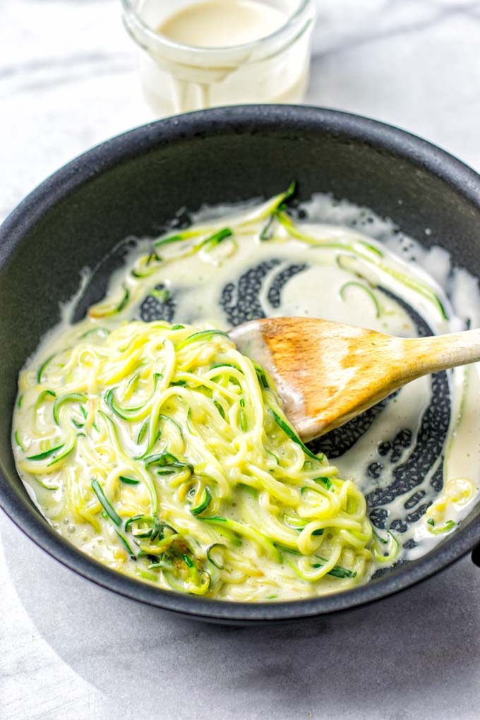 Combining the vegan Alfredo sauce with the zucchini noodles in a sauce pan.