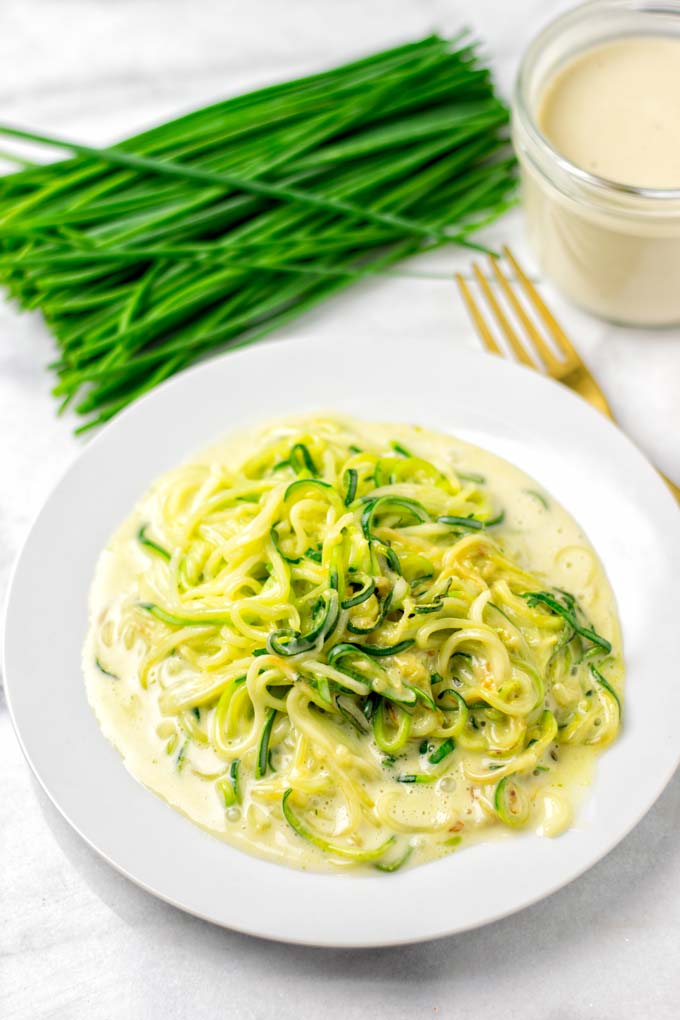 Serving the mixed zoodles and sauce on a white plate.