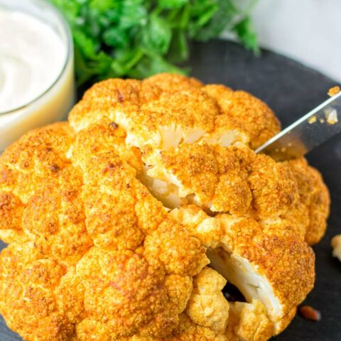 Knife cutting into the Roasted Cauliflower Head. A single portion is about a quarter of a head.