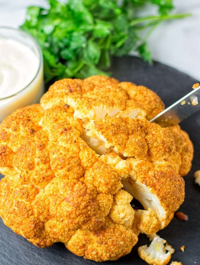 Knife cutting into the Roasted Cauliflower Head. A single portion is about a quarter of a head.