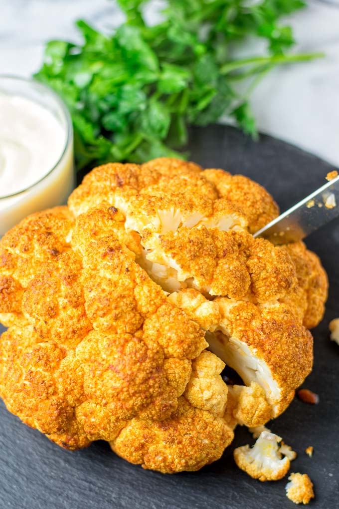 Knife cutting into the Roasted Cauliflower Head. A single portion is about a quarter of a head.