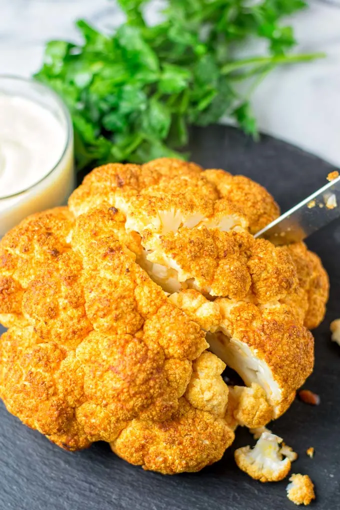 Knife cutting into the Roasted Cauliflower Head. A single portion is about a quarter of a head.