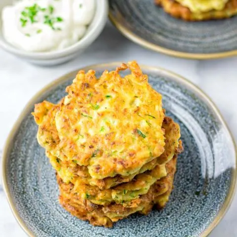 Stack of Zucchini Fritters on a blue plate with a small bowl of dip in the background.